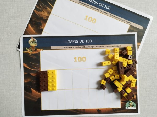 Tapis de nombres avec la décomposition progressive du nombre 100 en centaines, dizaines et unités, accompagné de cubes pour aider les élèves de CE1 à visualiser les différentes parties du nombre.